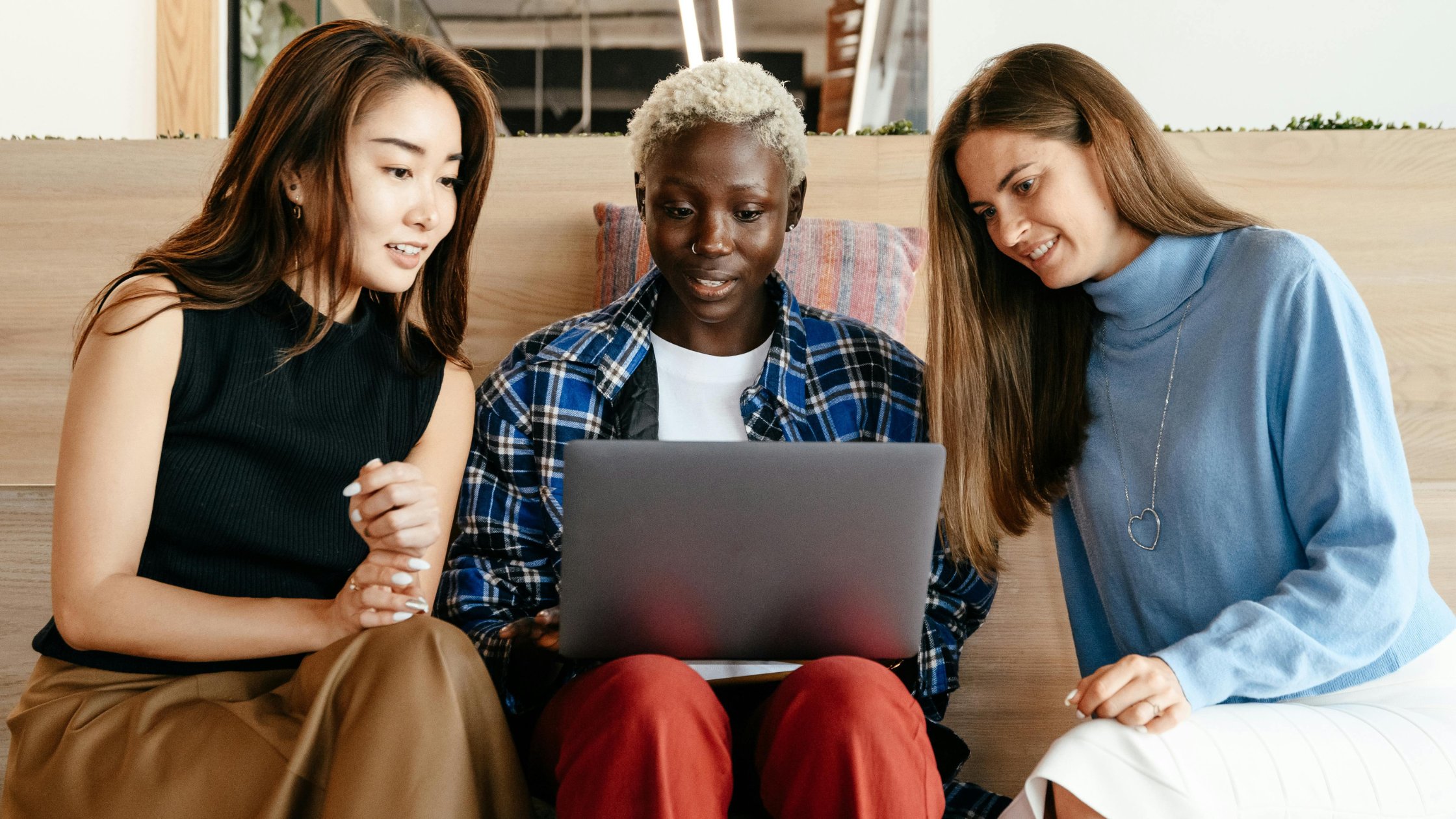 Three diverse individuals sitting together, collaborating while looking at a laptop. The setting appears casual and professional, indicating teamwork and shared insights.